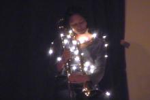 Rajni plays a trombone covered in fairy lights, still from documentation of 'As If Traveling Through Snow'